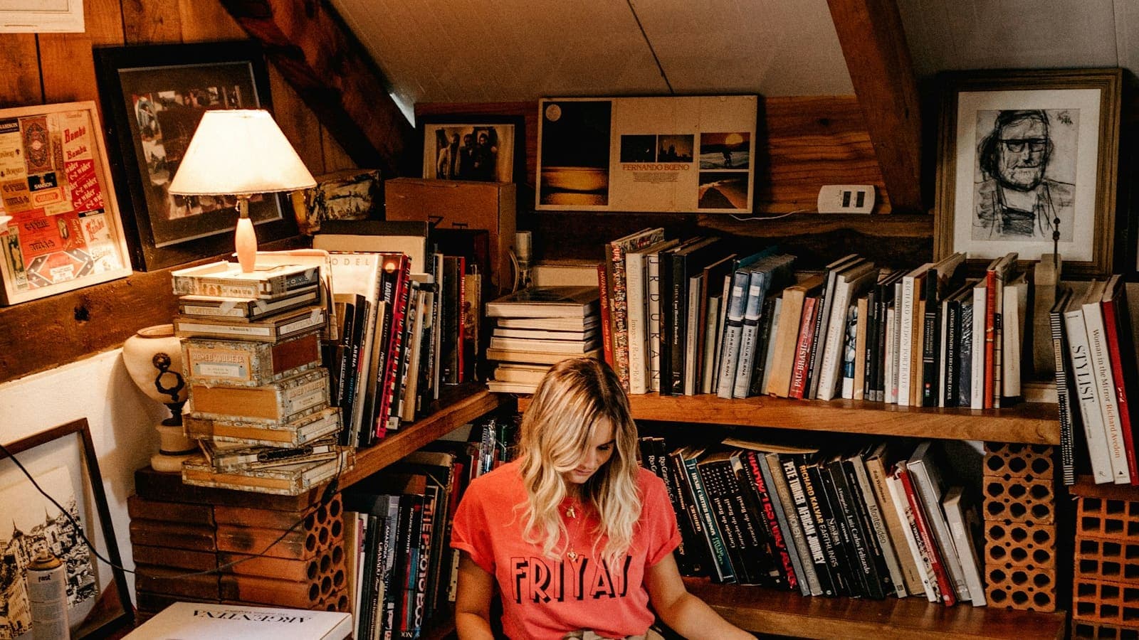 Un coin de lecture encombré de livres, éclairé par une lampe à abat-jour